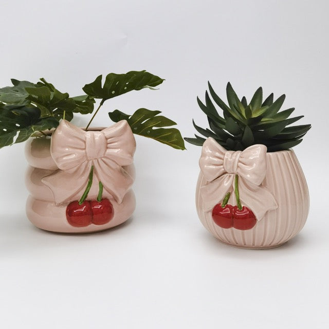 Two pink ceramic planters with bow designs and cherries on a white background