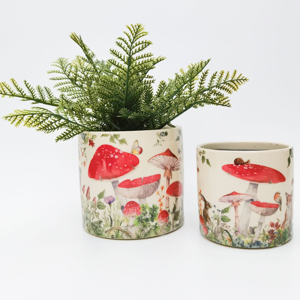 Two cylindrical planters with a whimsical design featuring red mushrooms and green foliage, containing small plants.