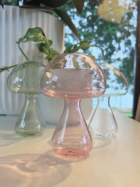 Three glass mushroom-shaped vases on a surface with a blurred outdoor background
