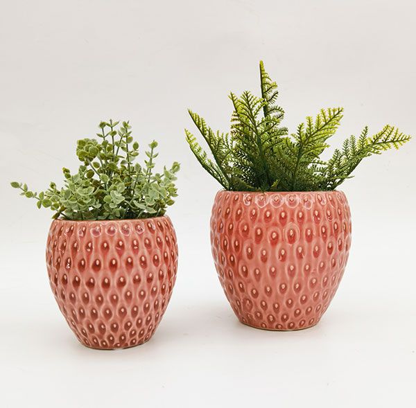 Two pink textured strawberry-shaped planters with green plants on a white background