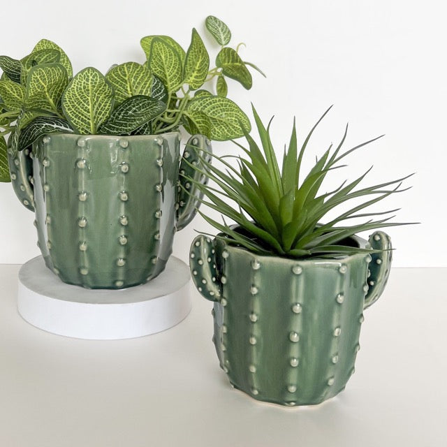 Two green cactus-shaped planters with plants on a white background