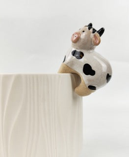 Ceramic cow perched on the side of a plant pot