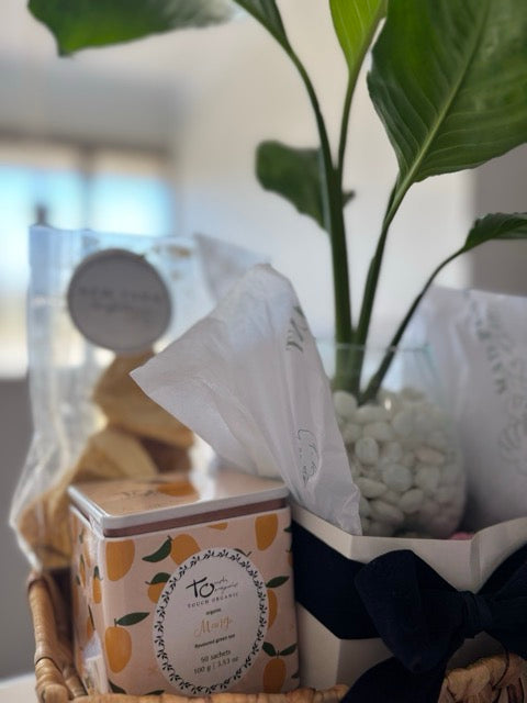 Candle in a decorative box with a plant and tissue paper in the background