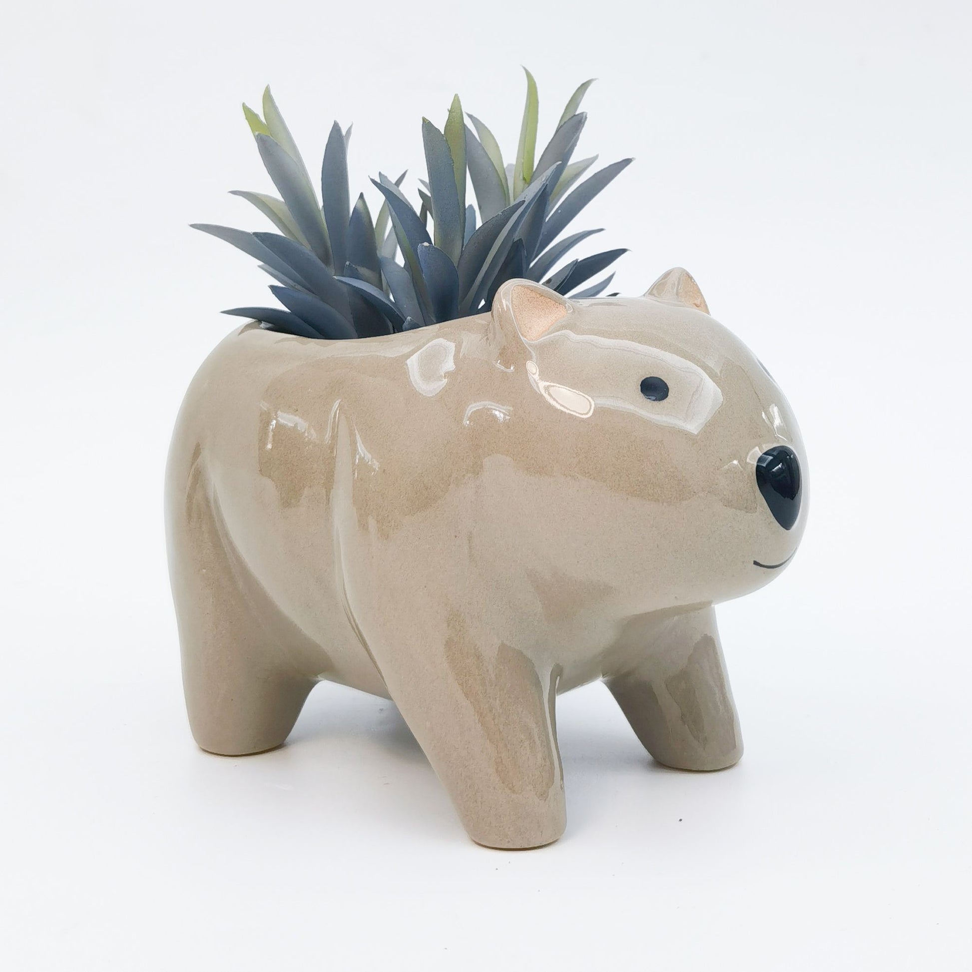 A beige ceramic wombat-shaped planter with a drainage hole and a few green plants sticking out of the top.