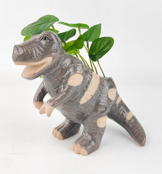 A T-Rex dinosaur-shaped planter in gray color with a small plant growing out of the top.