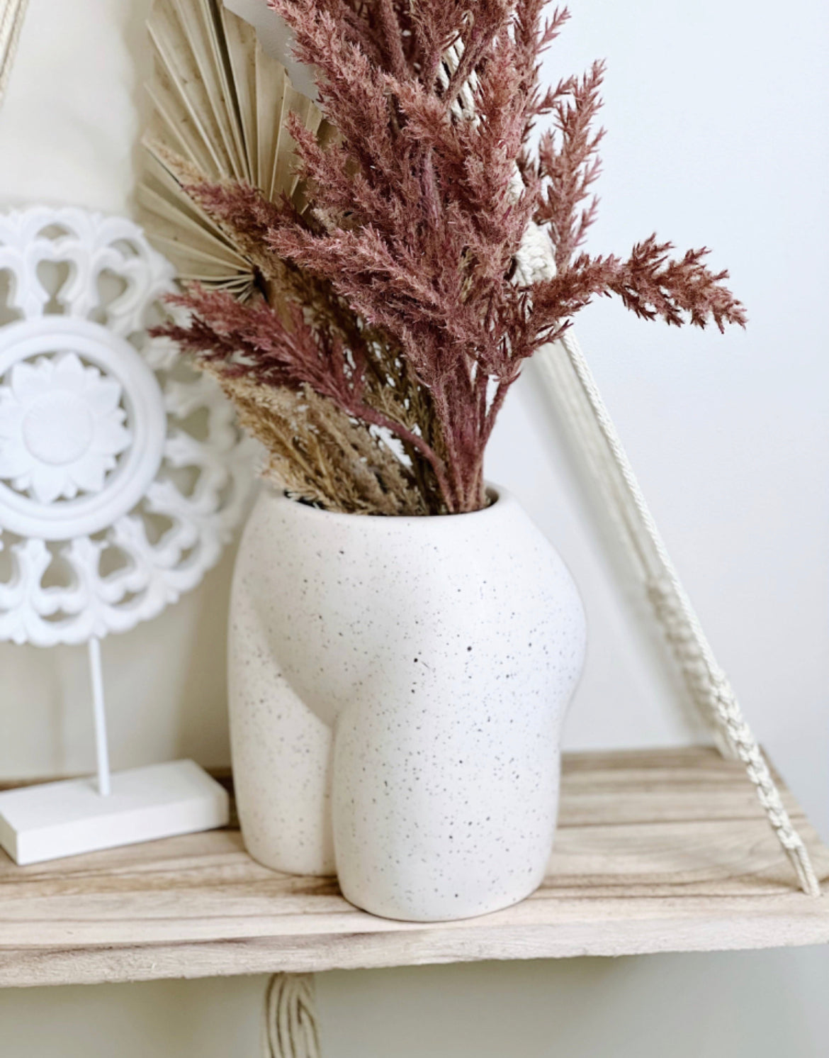 A beige ceramic vase with a playful, body-shaped design, resembling a bum, placed against a white tiled background.
